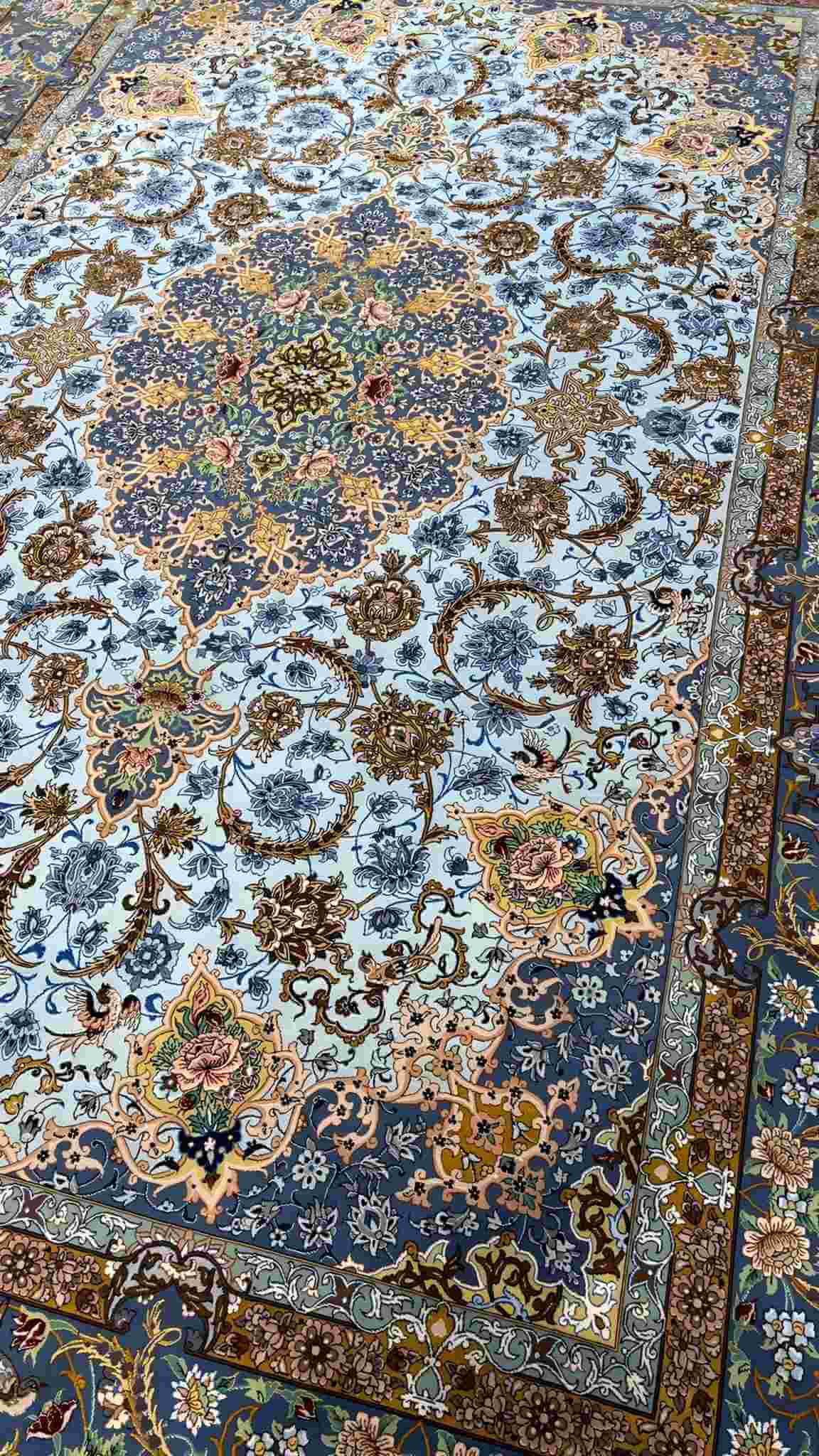 "Close-up of intricate floral designs on a light blue wool and silk Persian carpet."