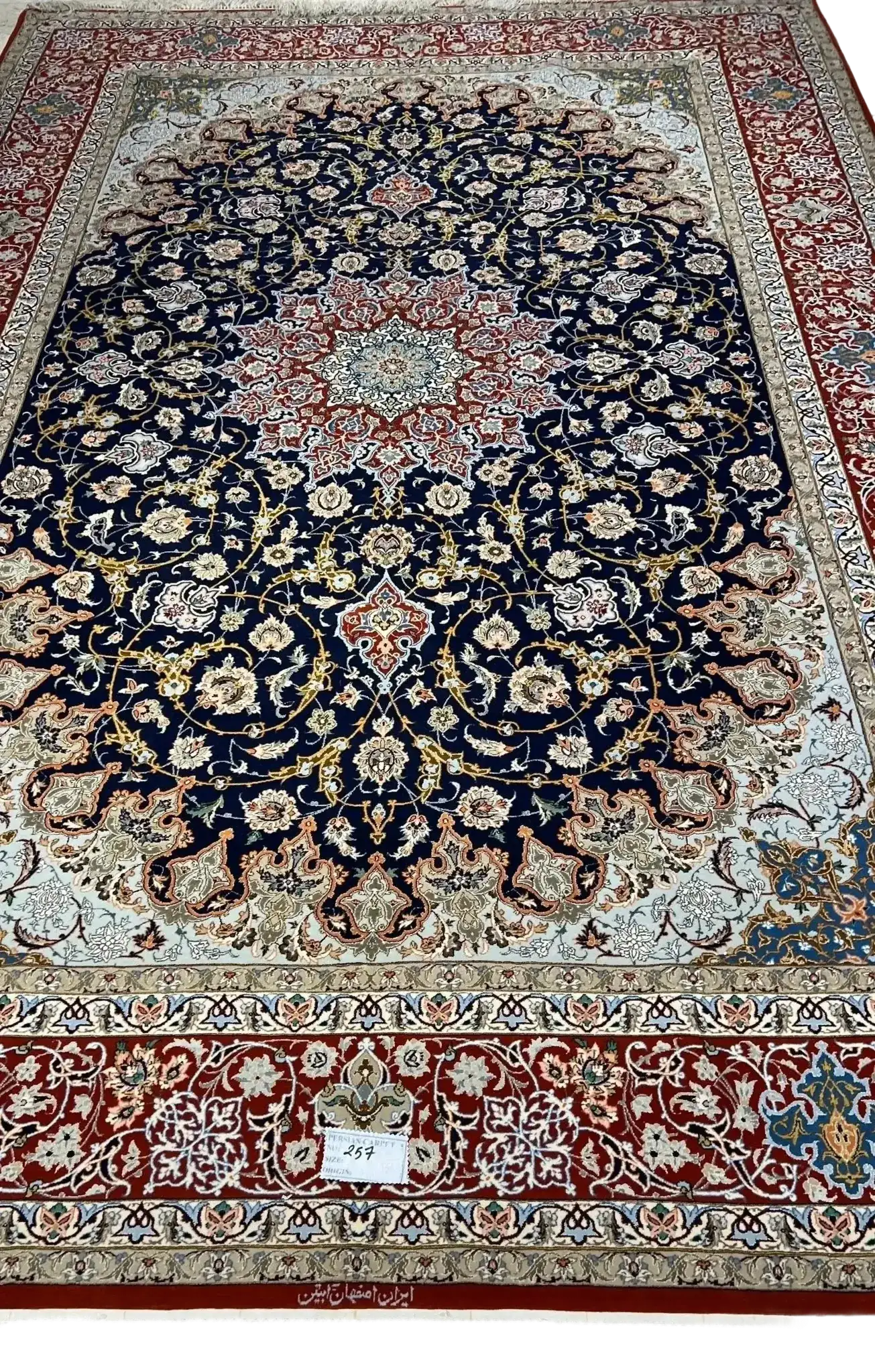 Intricate Floral Borders on Isfahan Carpet – A detailed image highlighting the intricate floral borders of a handmade Isfahan Persian rug, featuring vibrant reds, blues, and golds that contrast with the dark background.

