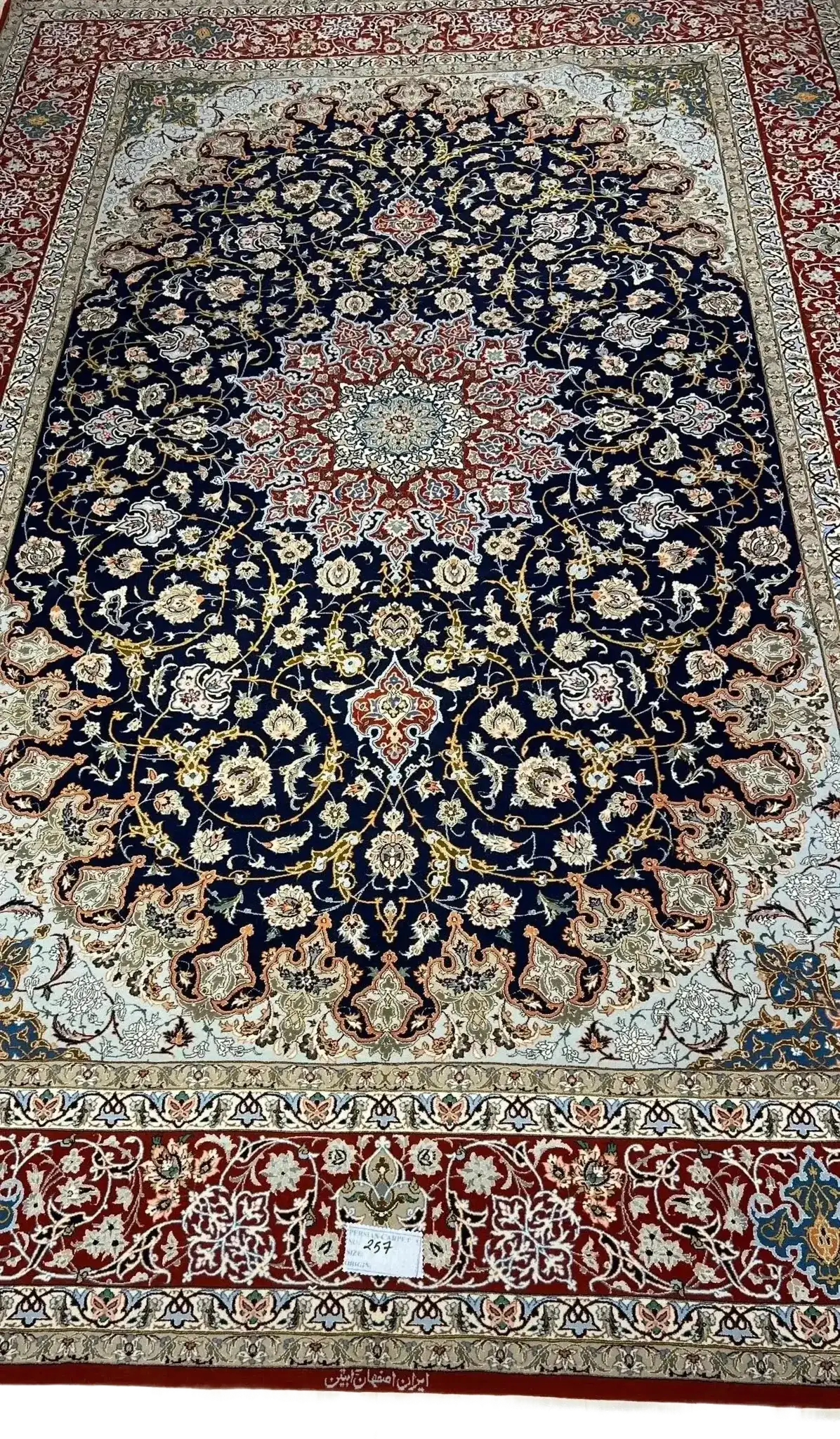 Handmade Persian Carpet from Isfahan – A full view of an elegant Persian carpet with a striking navy-blue field and intricate floral medallion design in red and ivory, hand-knotted with silk and wool by skilled artisans from Isfahan.

