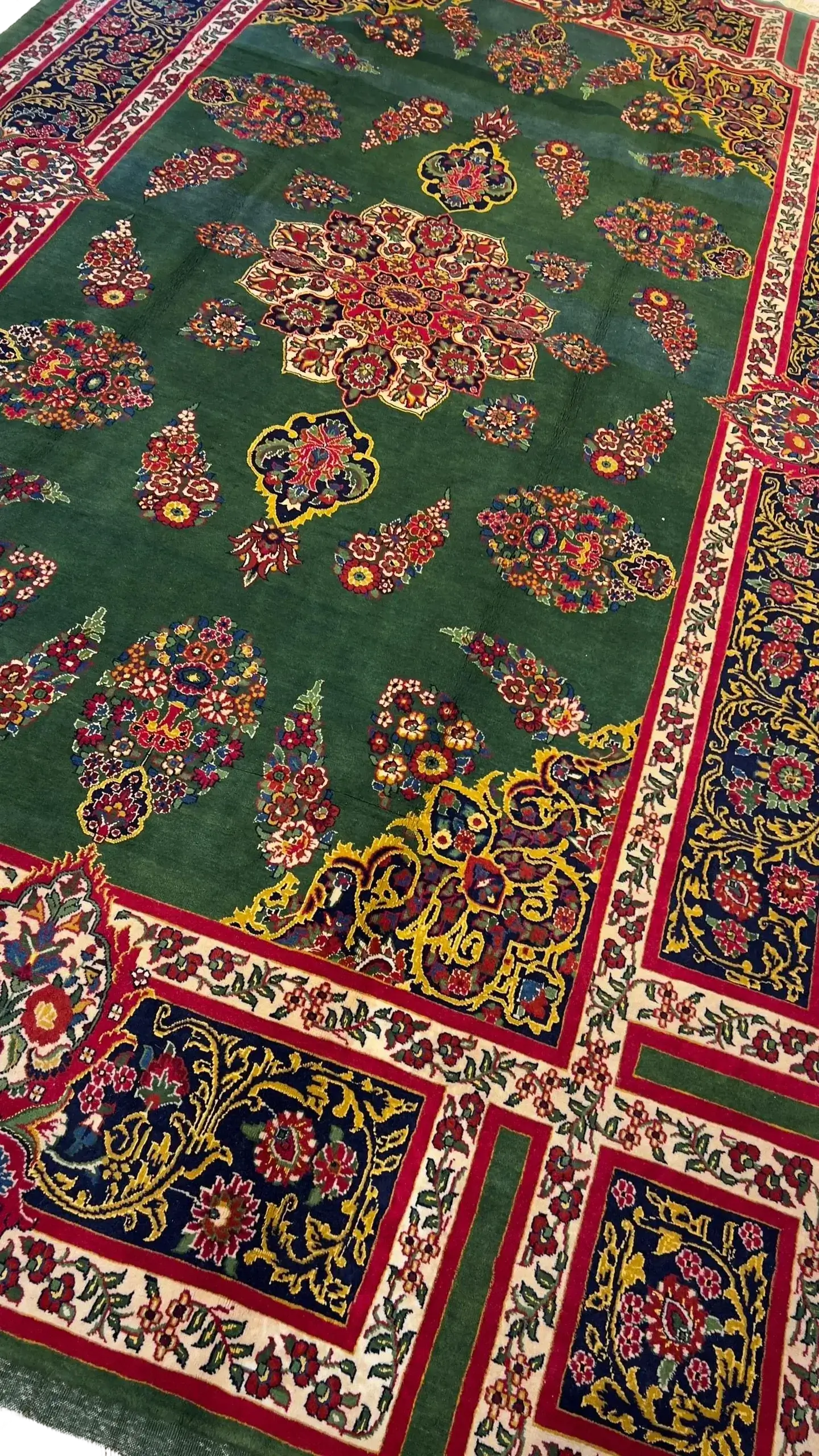 A detailed view of a Mashad rug with green and red patterns and floral accents