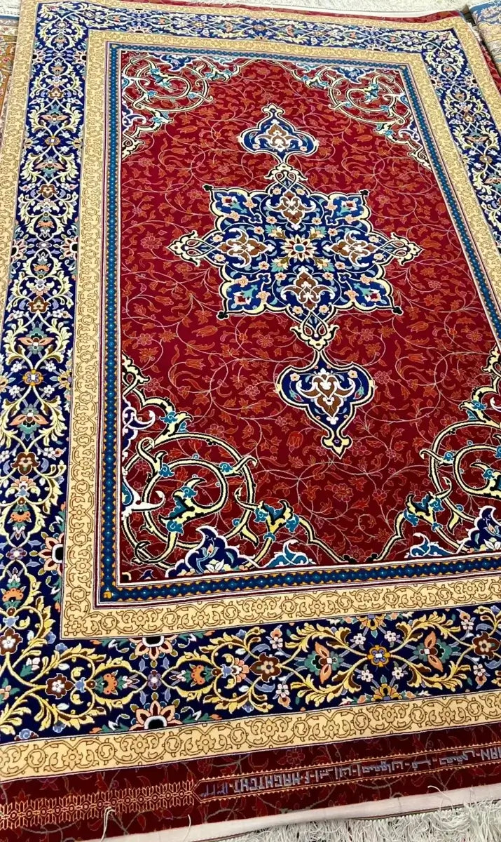 Wool and Silk Persian Area Rug - A close-up of the borders of a Persian rug, showcasing its intricate blue and gold patterns with floral motifs on a red base, woven with silk and wool.

